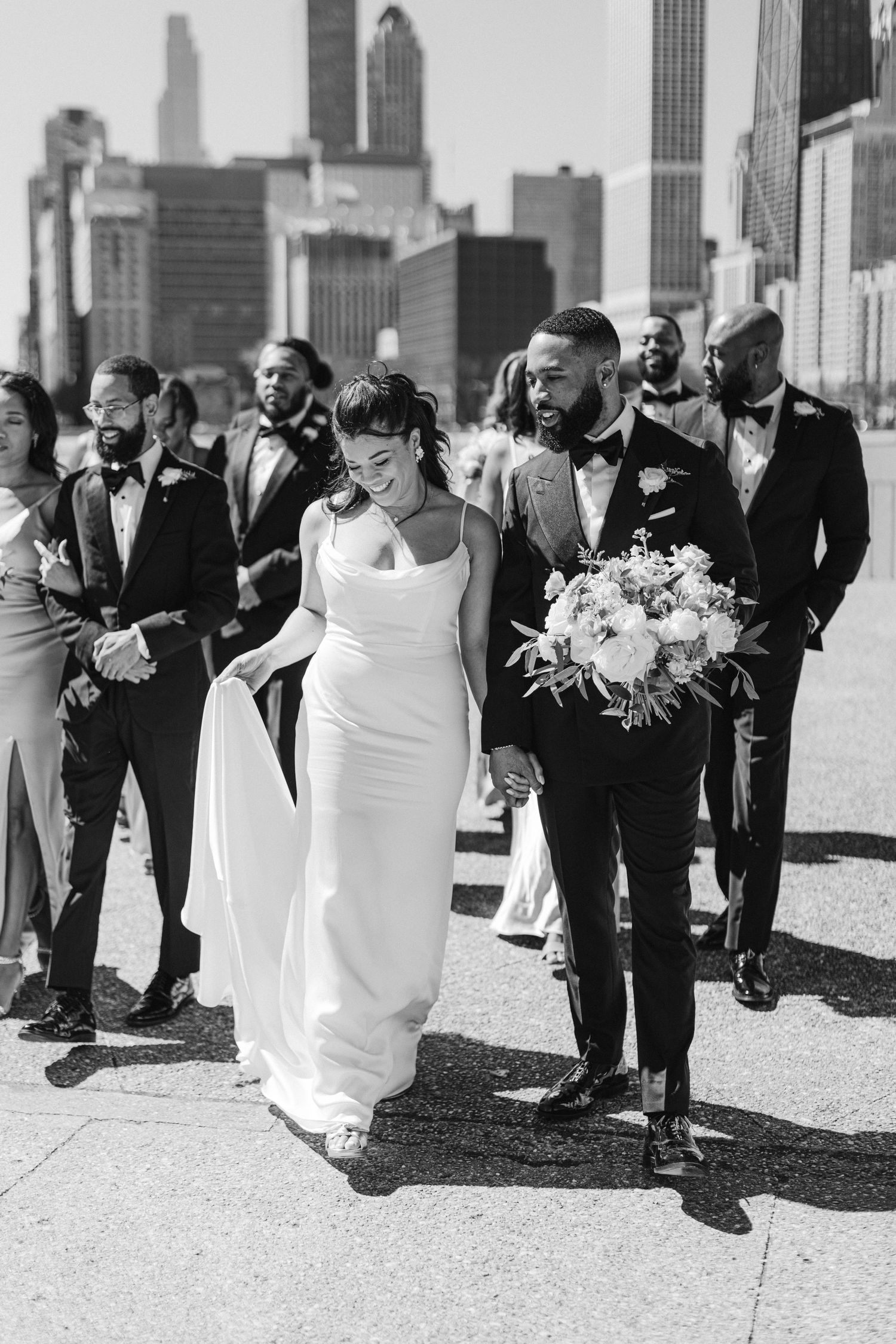 Wedding party walks along Chicago waterfront with city skyline in background.