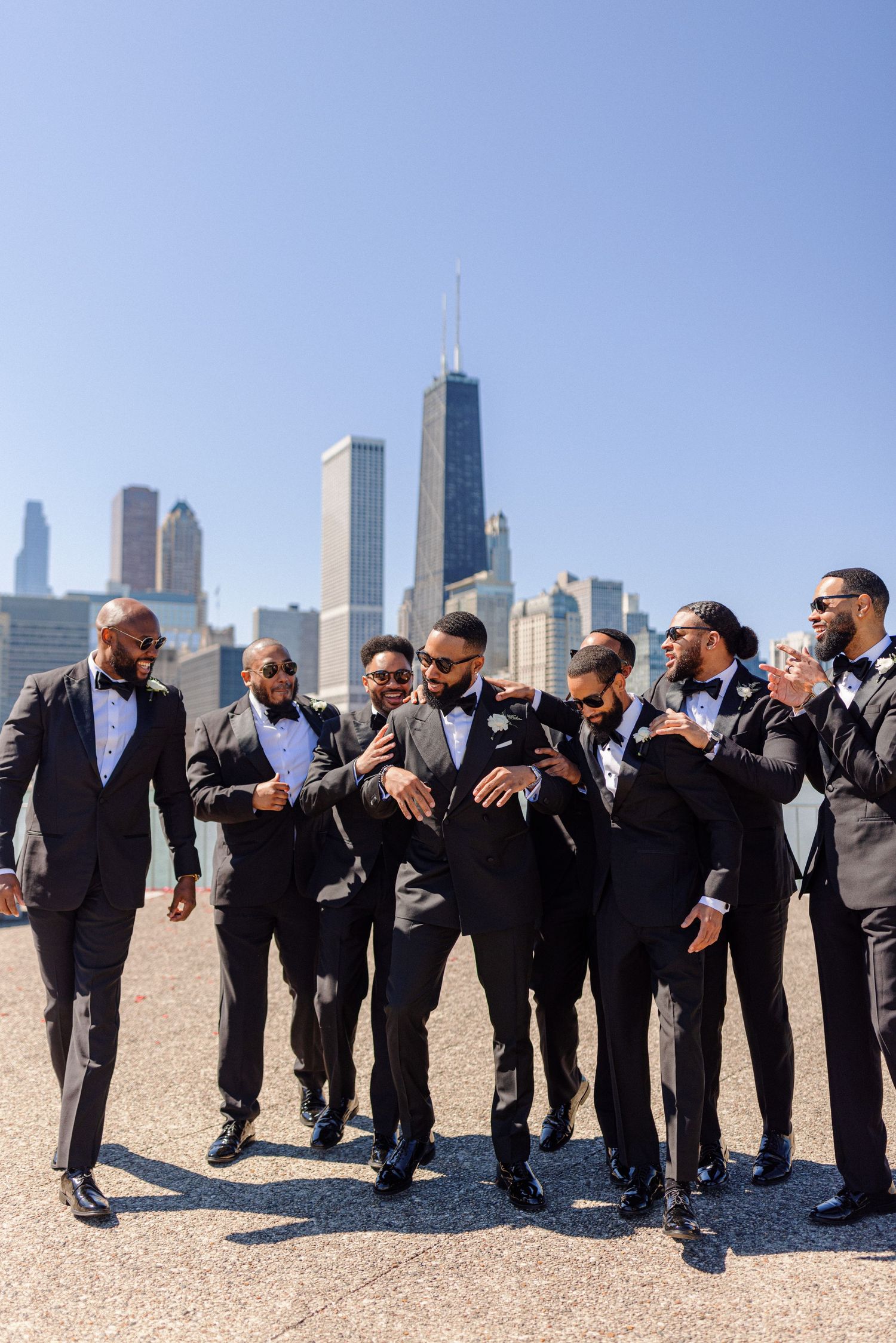Groomsmen in tuxedos pose together against Chicago skyline backdrop.