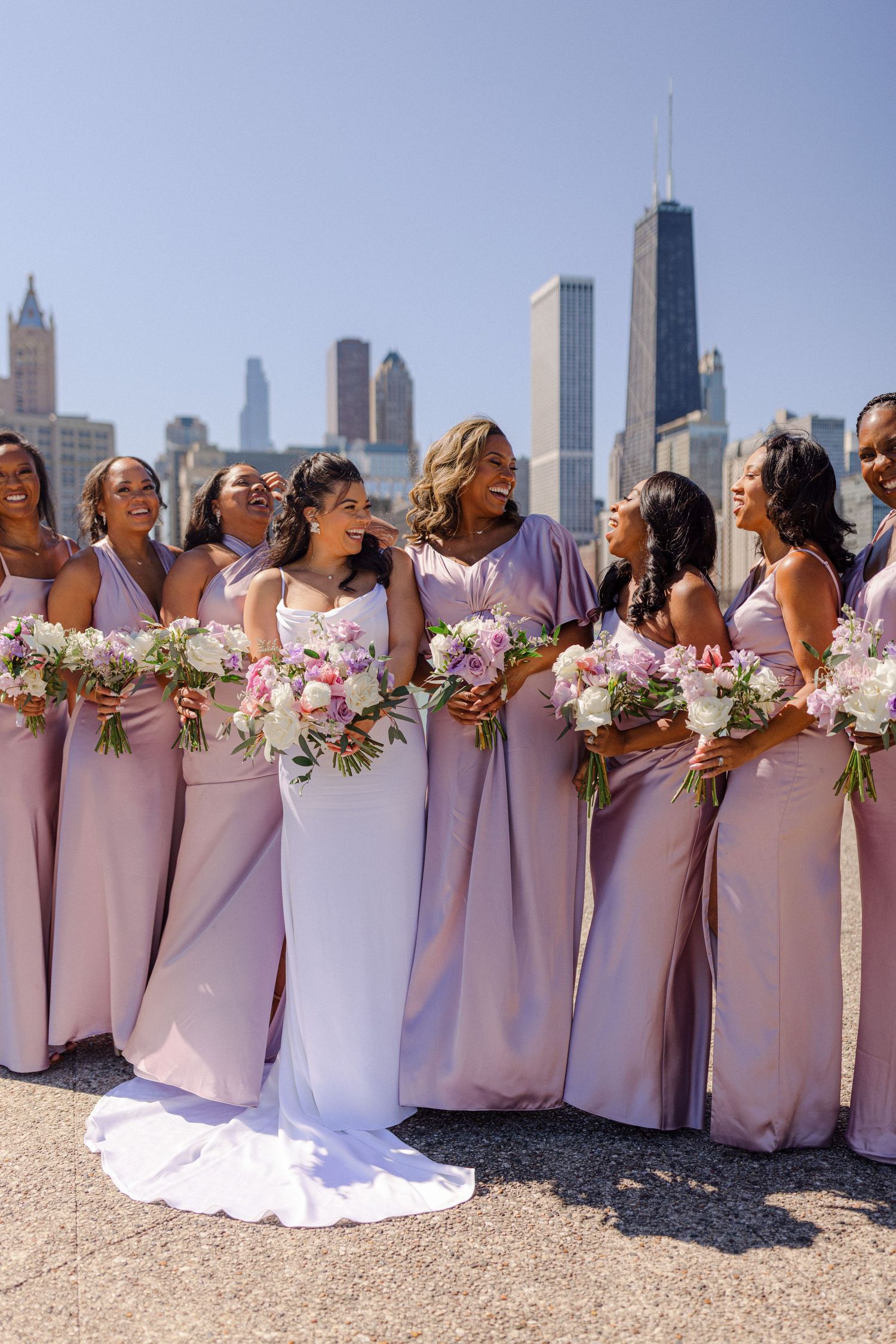 Bridal party in pink dresses poses with bouquets against Chicago skyline.