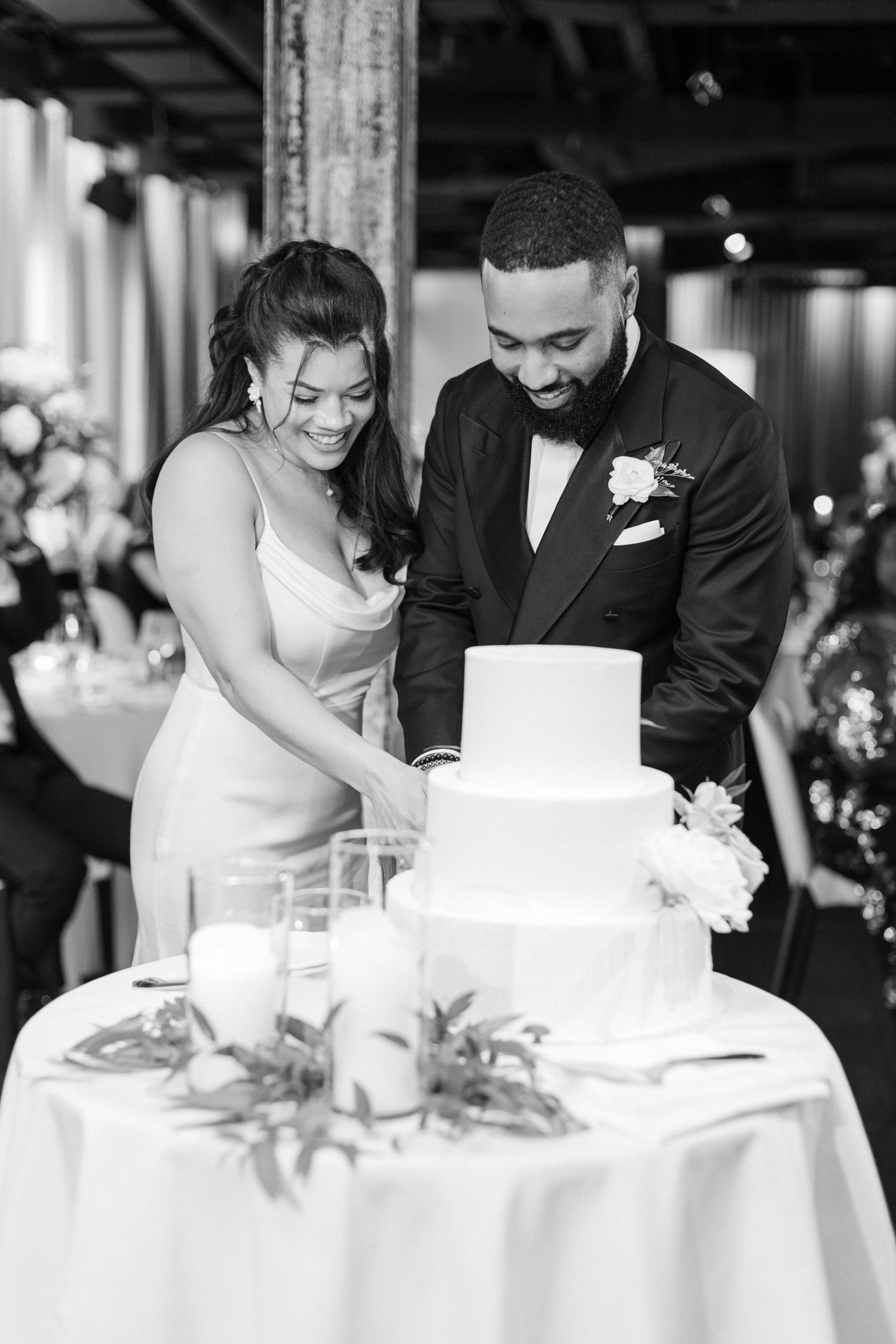 Couple sharing a joyful moment while cutting their elegant white wedding cake during reception.