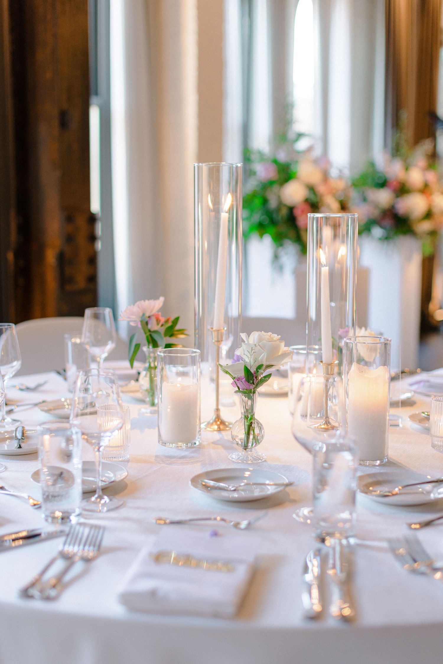 Minimalist wedding table setting with tall glass candleholders and delicate floral accents.