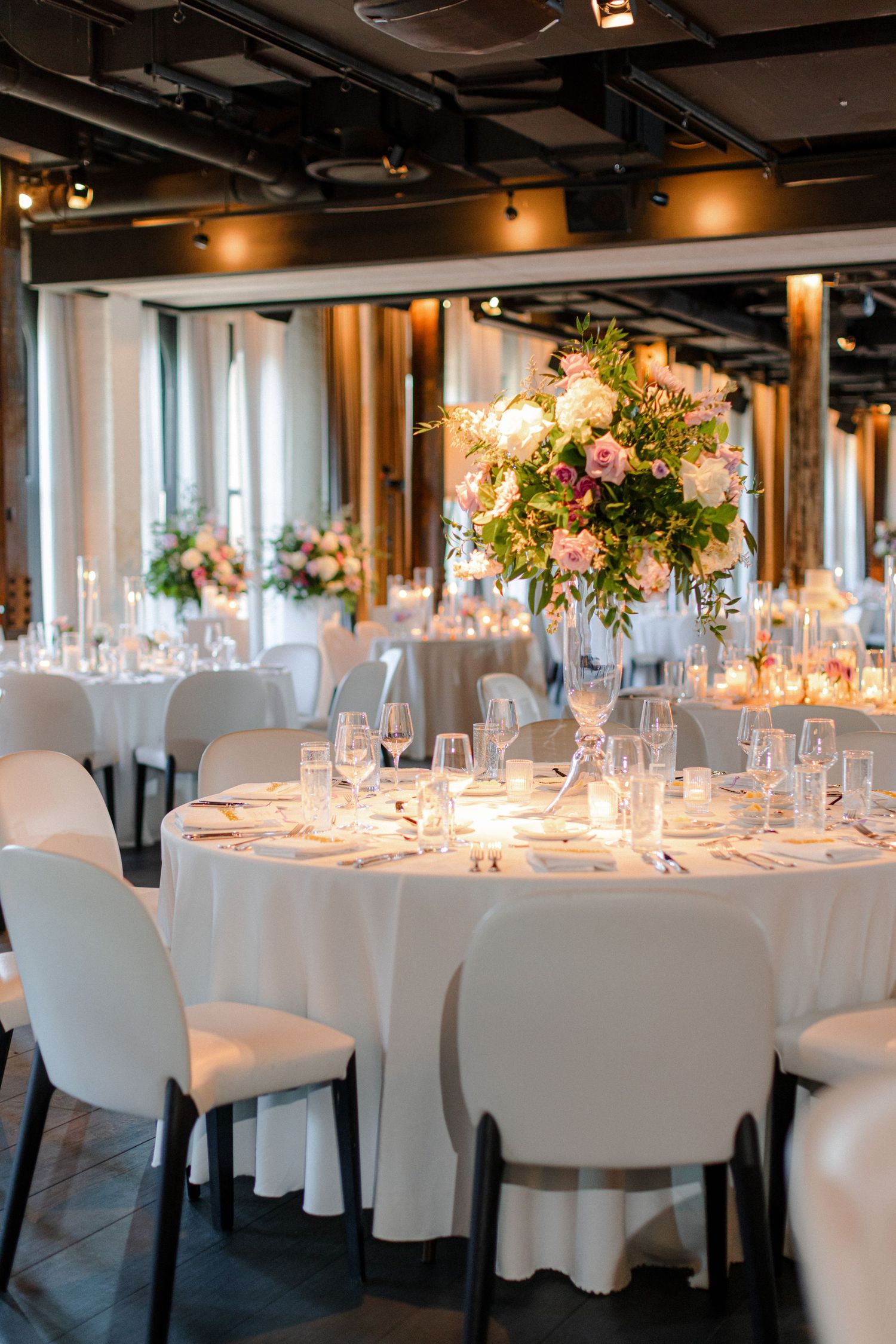 Modern wedding reception setup with white round tables, modern chairs and dramatic floral centerpieces.