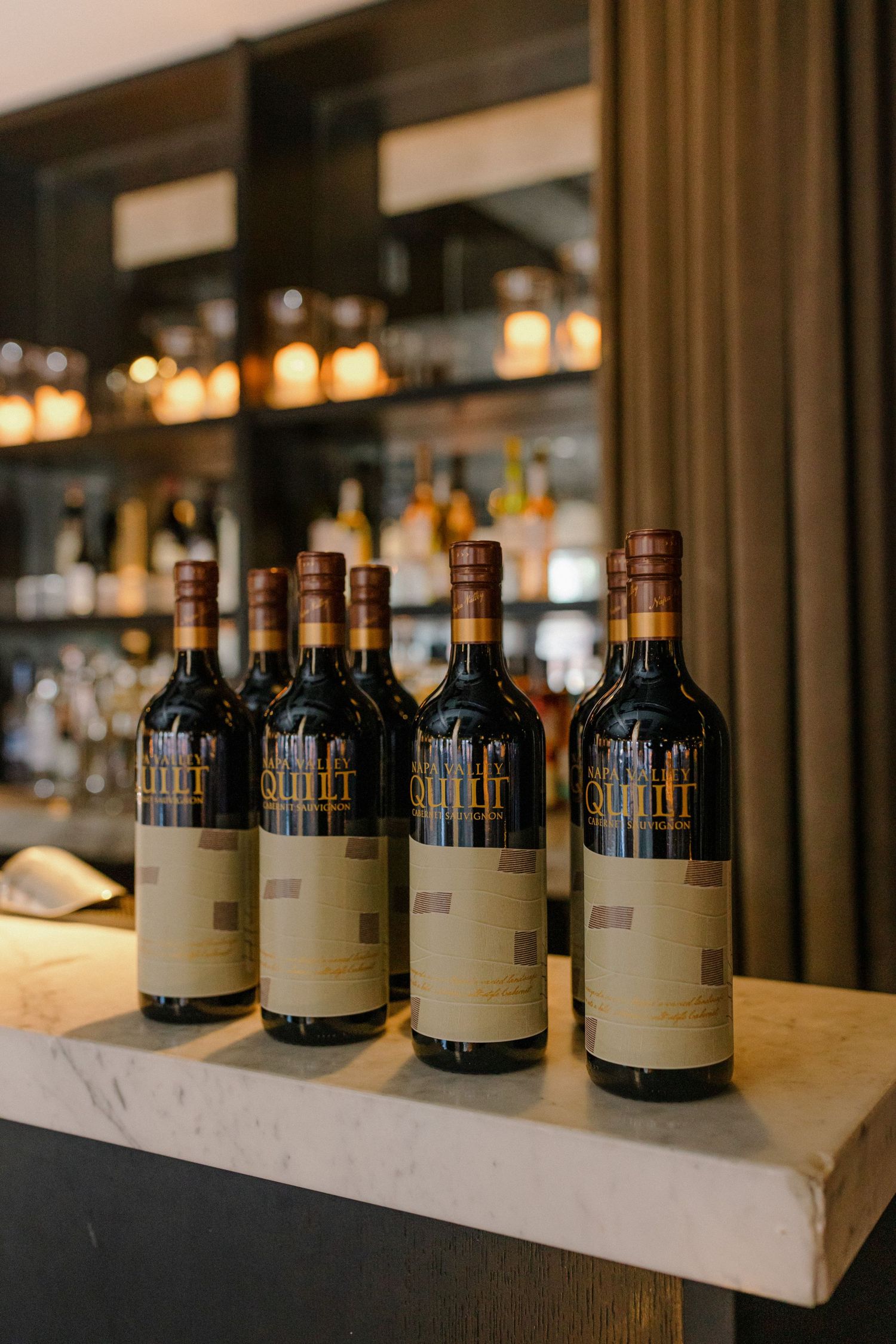 Row of wine bottles displayed on a marble bar counter with warm ambient lighting.