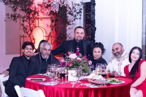 Group dining at a round table with red tablecloth and floral centerpiece at formal event.
