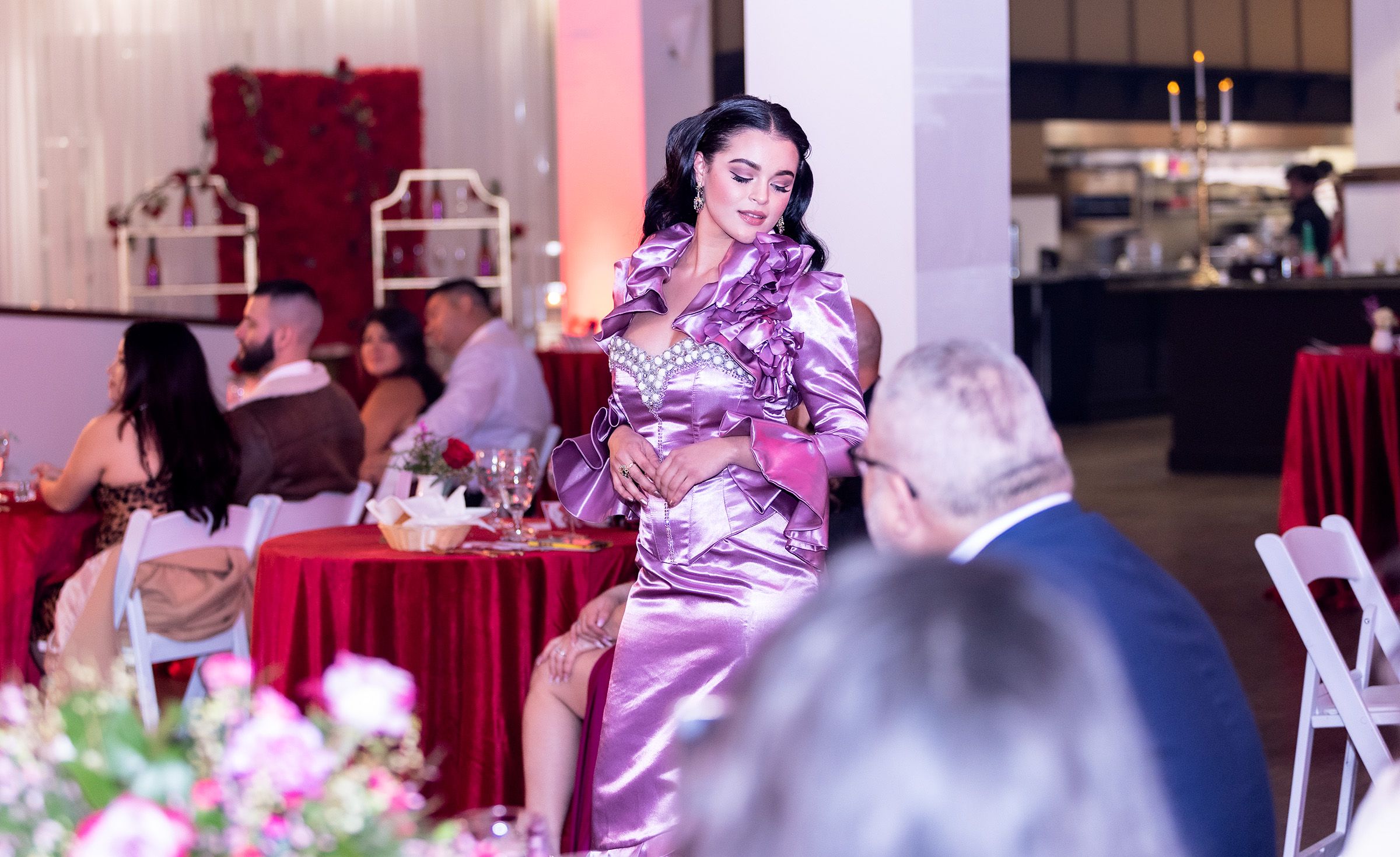 Guest in a purple dress stands among dining tables decorated with floral centerpieces at an elegant event.