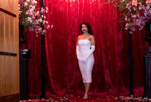 White dress against red velvet backdrop with cherry blossom floral arrangements.