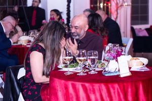 Guests enjoy an intimate dinner conversation at a formal event with red tablecloths and wine glasses.