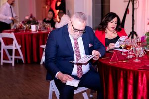 Guest reading program materials at formal dinner with red tablecloth decor.