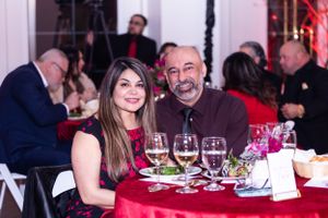 Guests enjoying wine and dinner at formal event with red tablecloth settings.