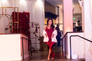 Stylish figure in a red dress poses confidently in an elegant hallway with pink lighting.