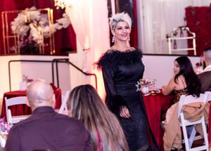 Elegant evening event with attendee in black feathered dress addressing seated guests.