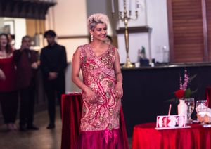 Formal event with woman in pink patterned dress standing near decorated tables.