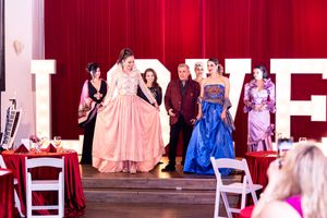 Performers in formal gowns on stage during a theatrical production.