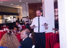 A server in a white dress shirt takes orders at a restaurant with red tablecloths.