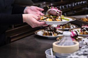 Server holds plates of elegantly plated food in a formal dining setting.