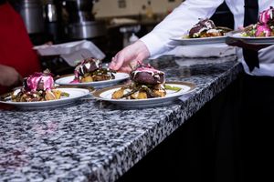 Chef plating elegant dinner dishes on marble counter at catered event.