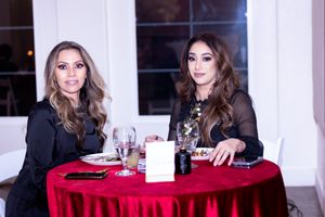 Two guests seated at round table with red tablecloth at formal dinner event.
