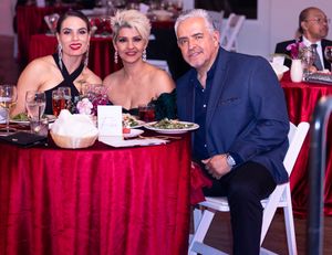 Guests enjoying dinner at a formal event with red tablecloths and table settings.
