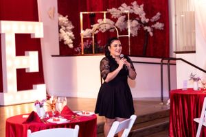 Speaker presenting at formal event with red decor and cherry blossom arrangements.
