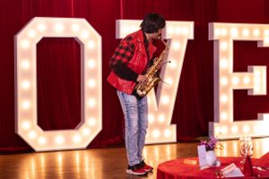 Musician plays saxophone in front of large illuminated LOVE letters on stage.
