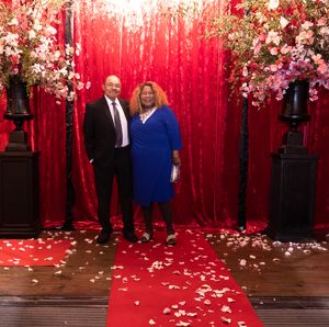 Red carpet photo backdrop with sparkly curtain, rose floral arrangements, and scattered petals creating an elegant setting.