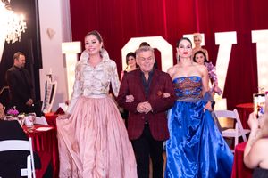 Models walk the runway in elegant pink and blue gowns at a glamorous fashion show event.