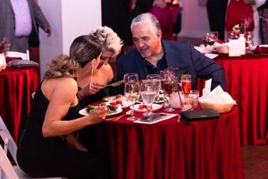 Diners seated at tables with red tablecloths enjoying their meals at an elegant event.