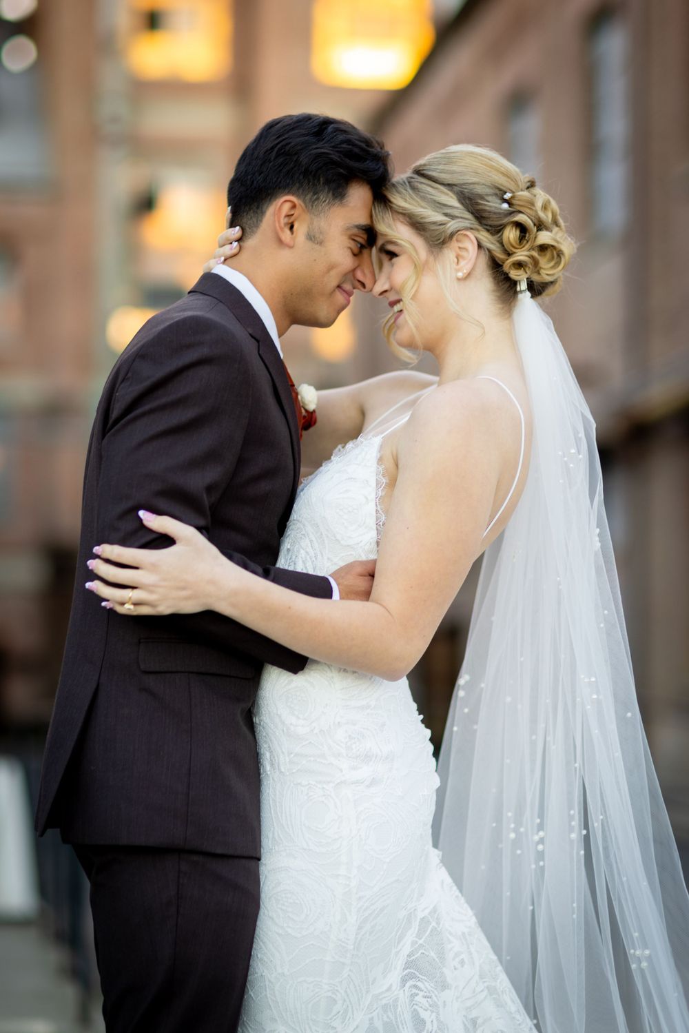 A romantic wedding portrait of newlyweds sharing an intimate moment against a brick building.
