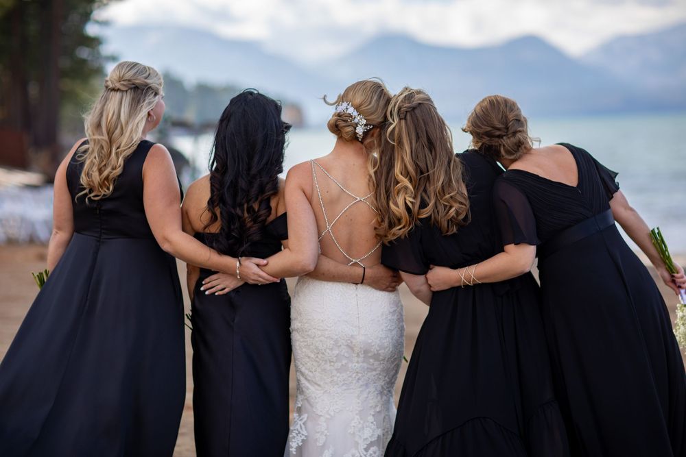 Bridesmaids in navy blue dresses stand arm in arm with the bride against a mountain backdrop.