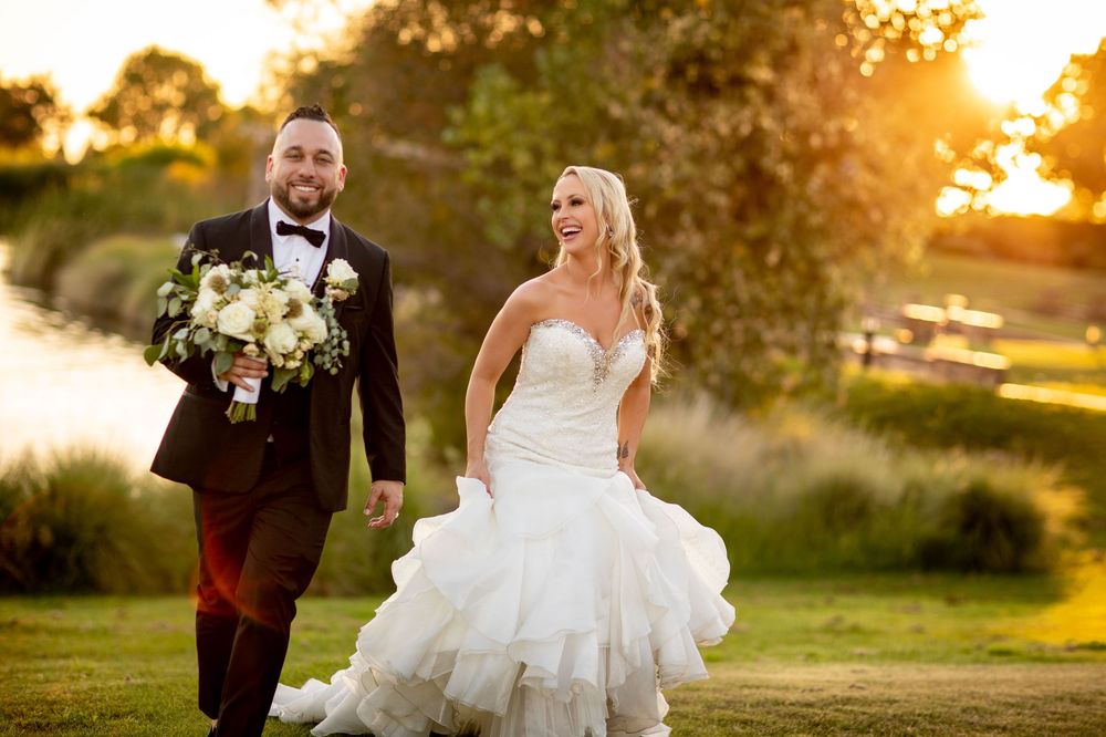 Wedding couple walks together in a golden sunset at a garden venue as the bride's white dress flows in the breeze.