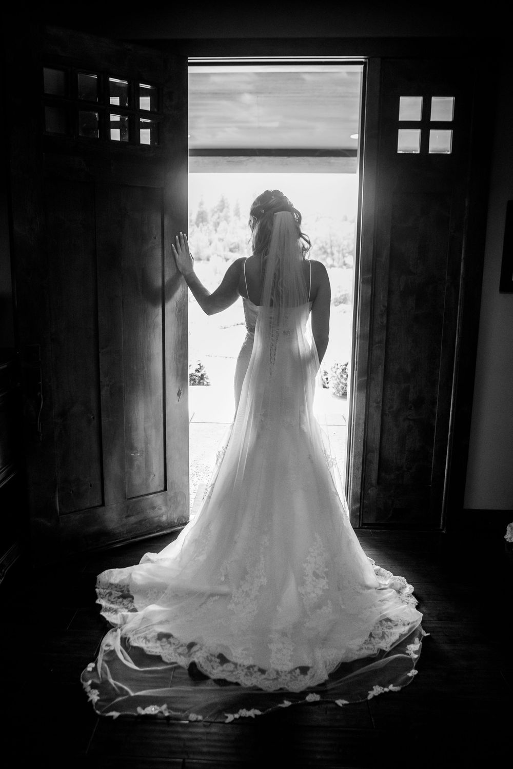 A silhouetted figure in a wedding dress stands in front of a bright window creating a dramatic backlit effect.