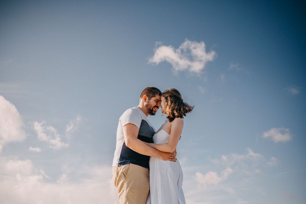 Couple sharing an intimate moment against a blue sky backdrop.