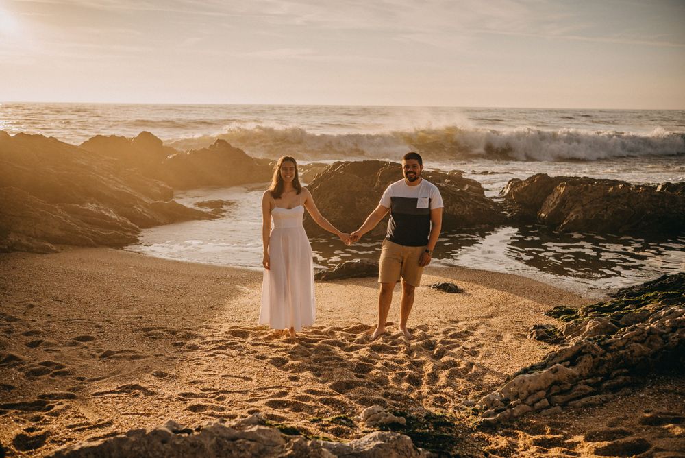 Couple holding hands on rocky beach during golden hour sunset.