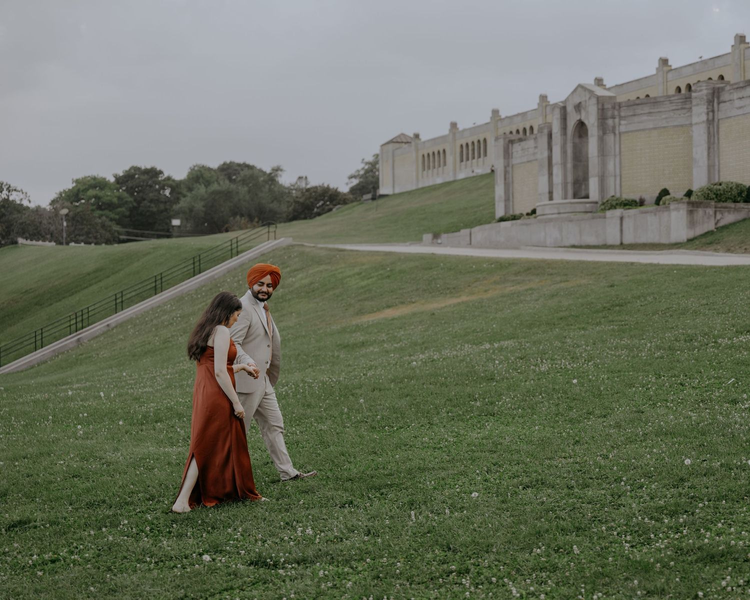 A couple strolling down a grassy hill near a grand white classical building.
