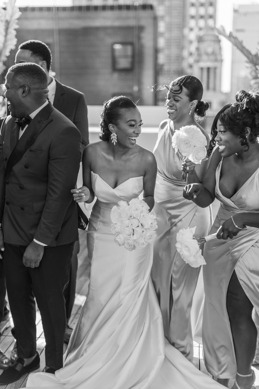 Black and white candid photo of wedding party sharing joyful moment together outdoors.