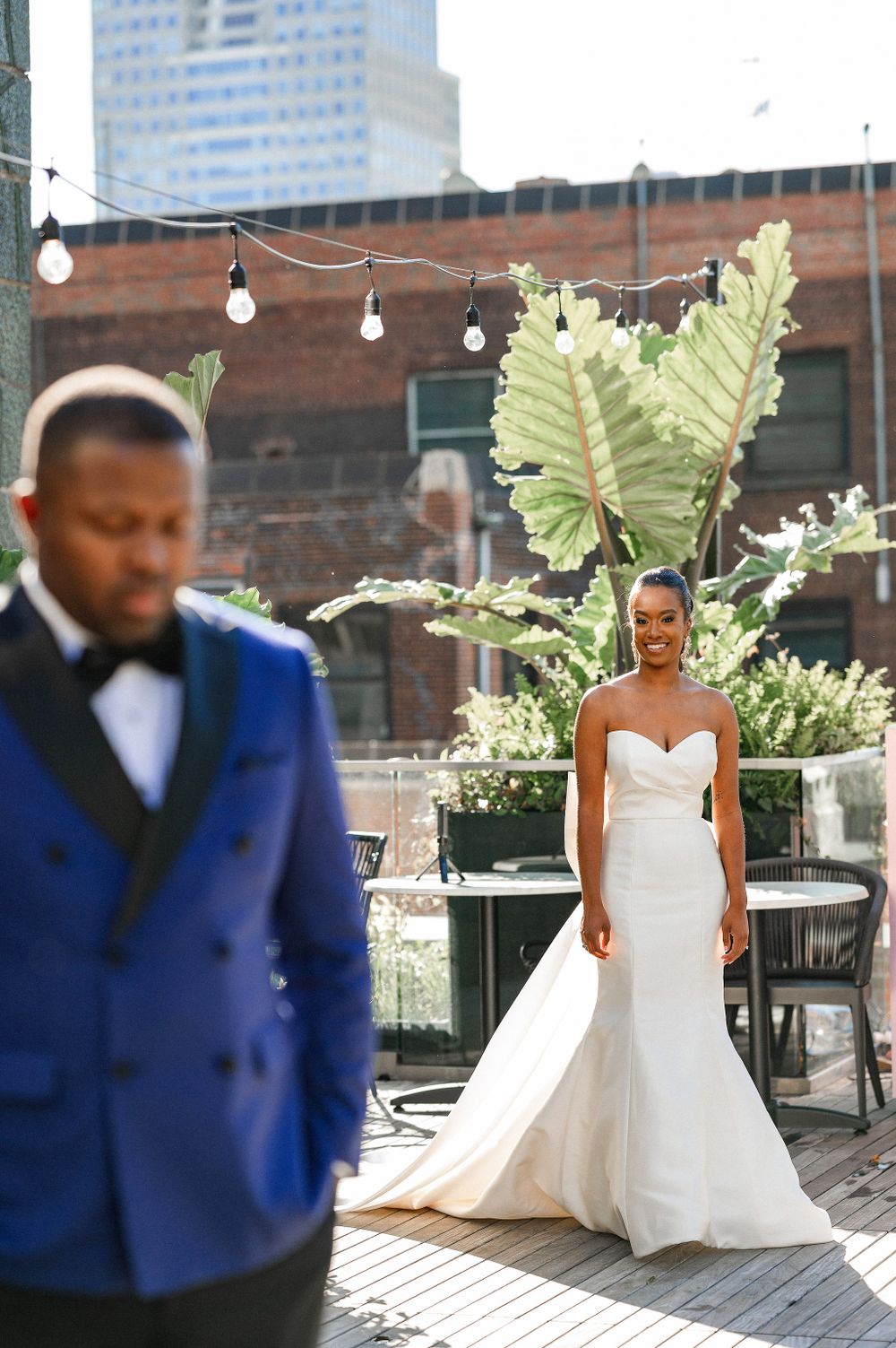 Elegant outdoor wedding photoshoot with tropical plants and string lights on city rooftop.