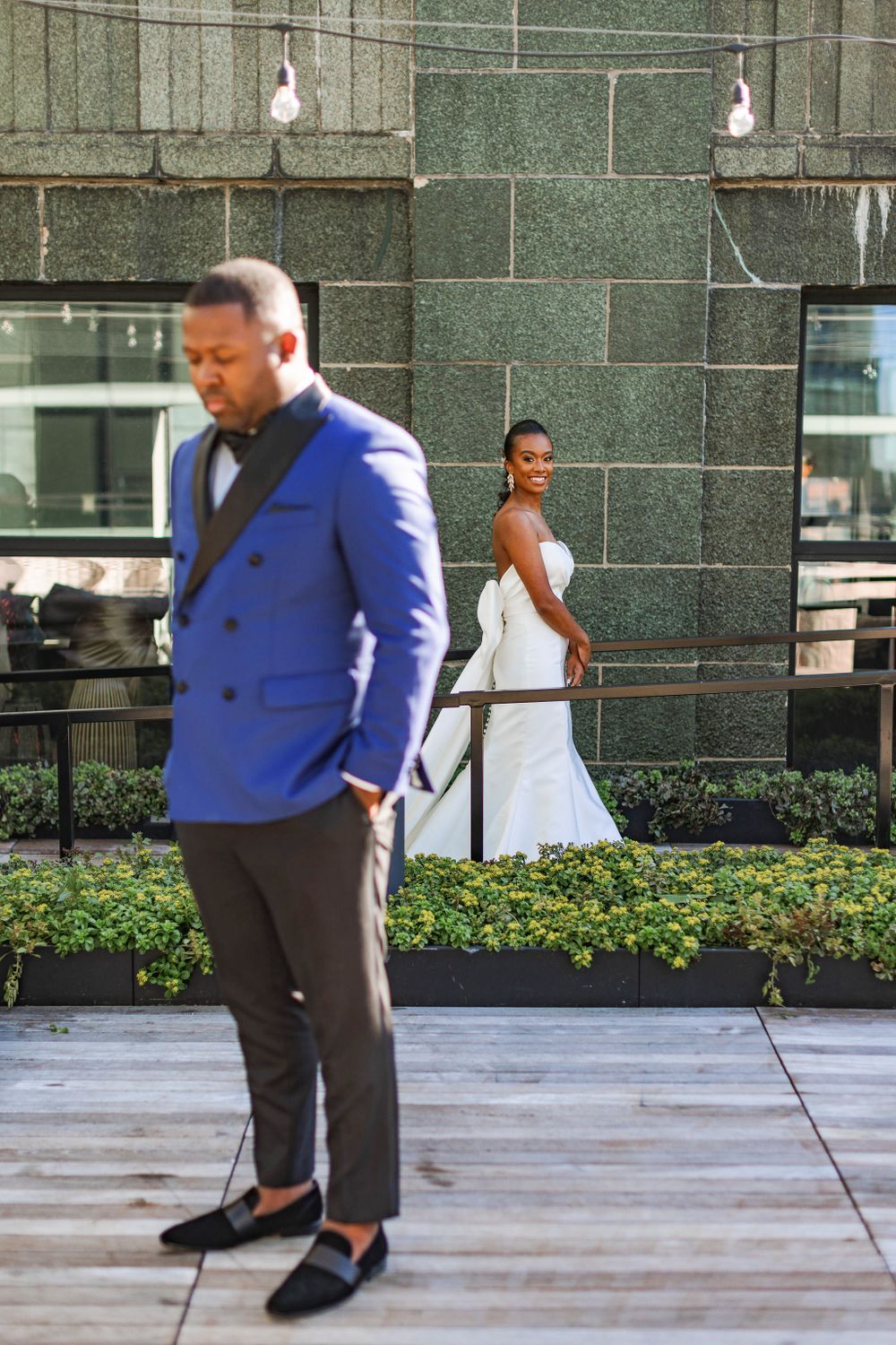 Wedding first look moment on rooftop terrace with groom in blue blazer and bride in elegant white dress.