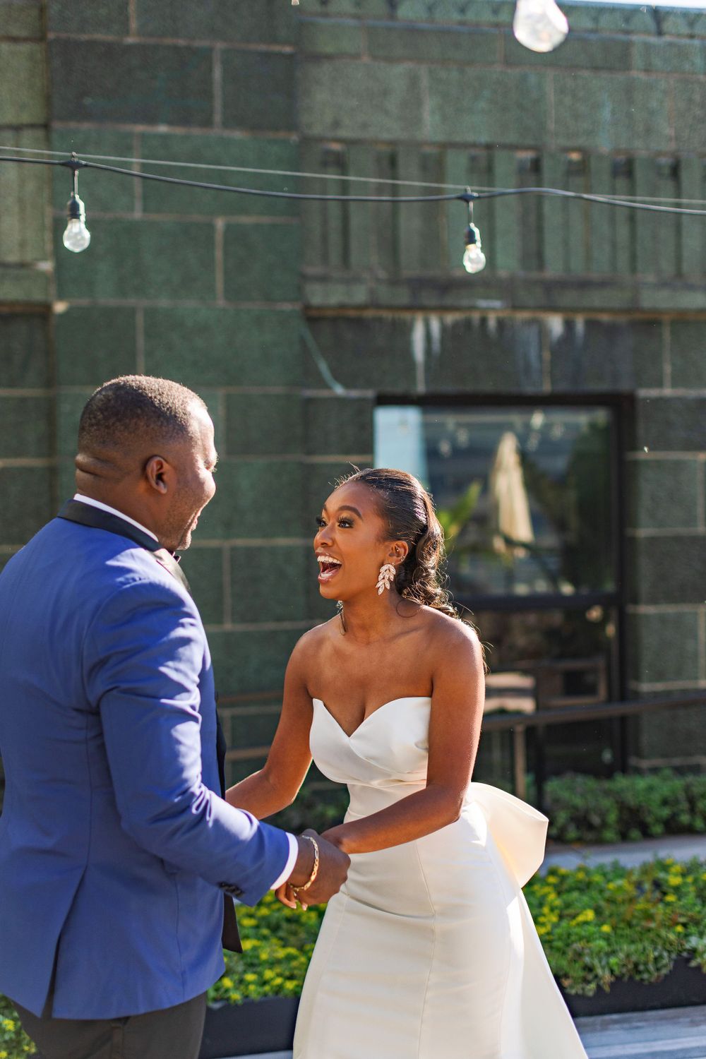Emotional wedding moment captured on urban rooftop with string lights and greenery.