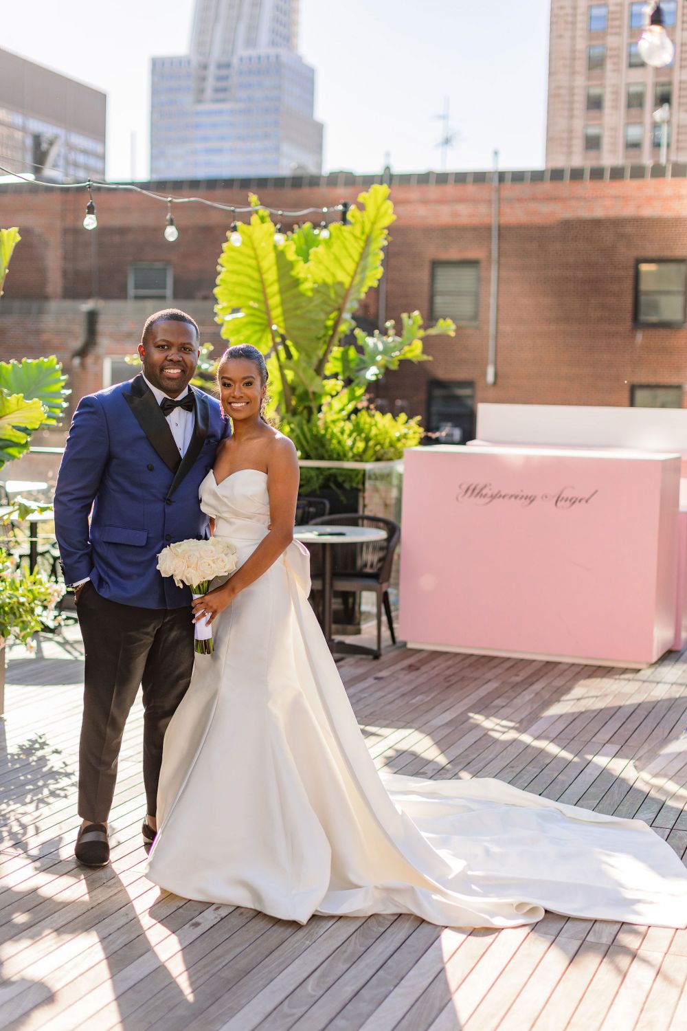 Rooftop wedding portrait with city backdrop and pink welcome sign.