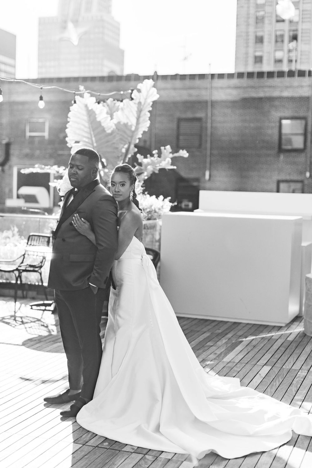 Black and white portrait of couple embracing on rooftop deck with city skyline.