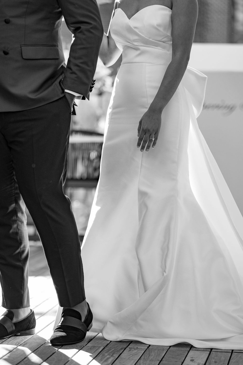 Black and white detail shot of wedding dress silhouette and groom's suit.