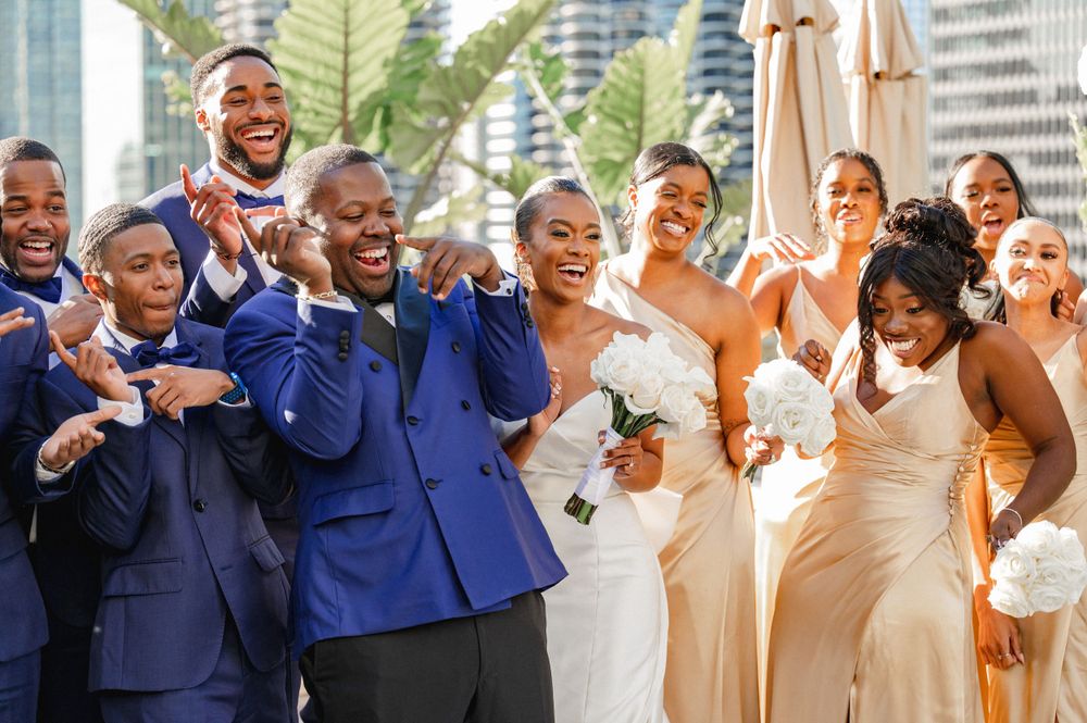 Wedding party in navy suits and cream dresses poses together outdoors with urban backdrop.