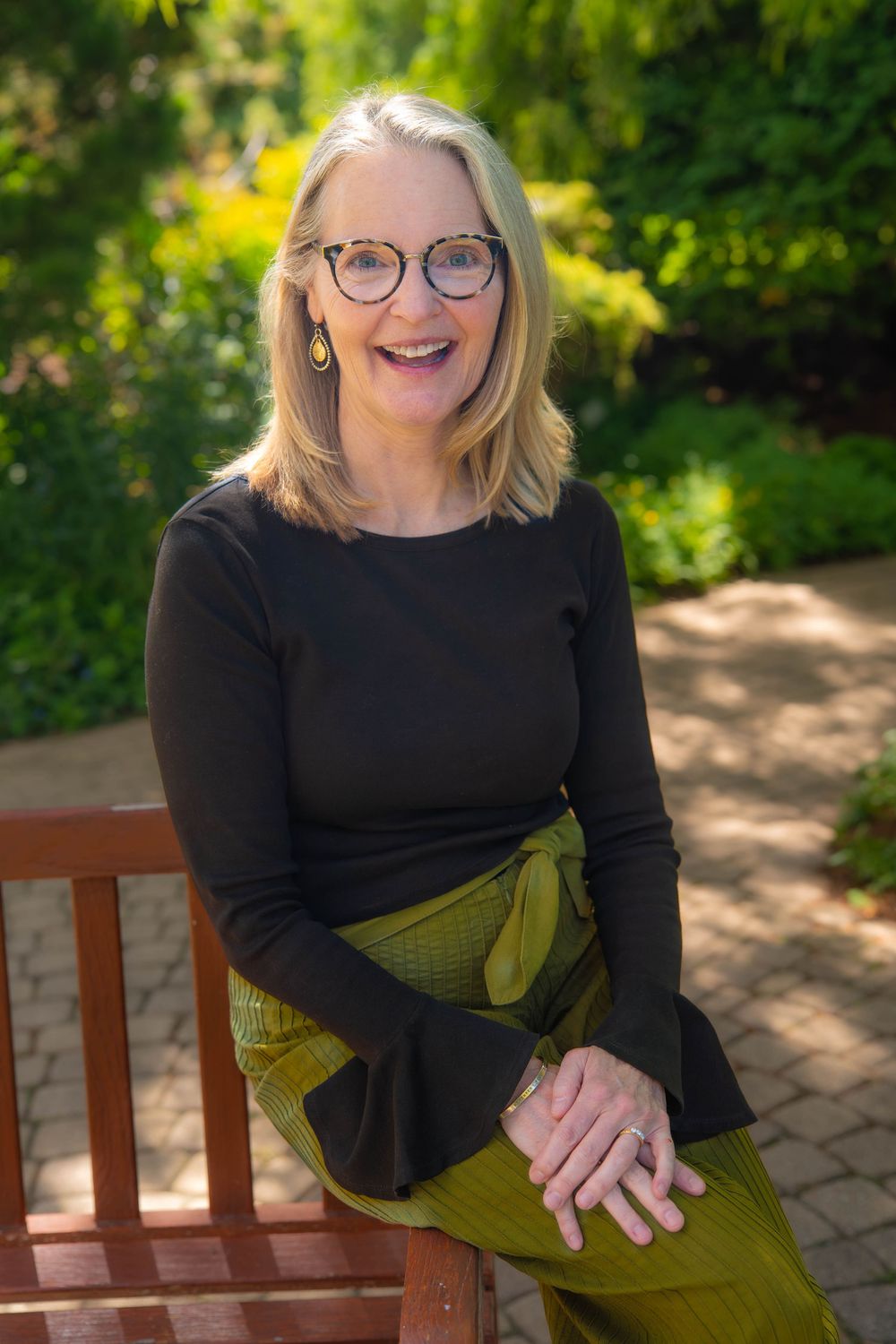 Casual portrait series on wooden bench outdoors with greenery background in black top and olive dress. Lifestyle Headshot Quad Cities