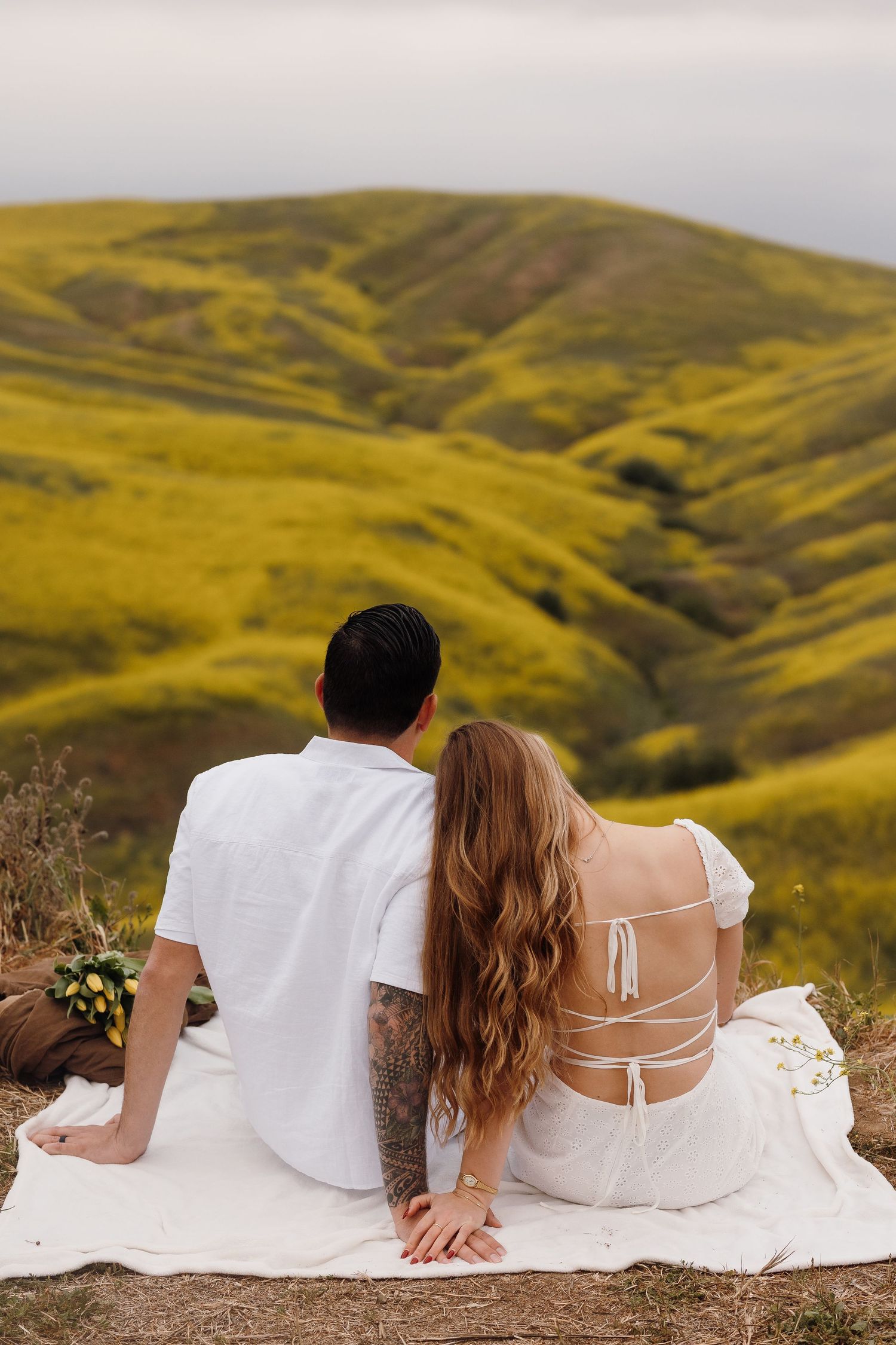 Couple sitting together on hillside blanket overlooking lush green rolling meadows.