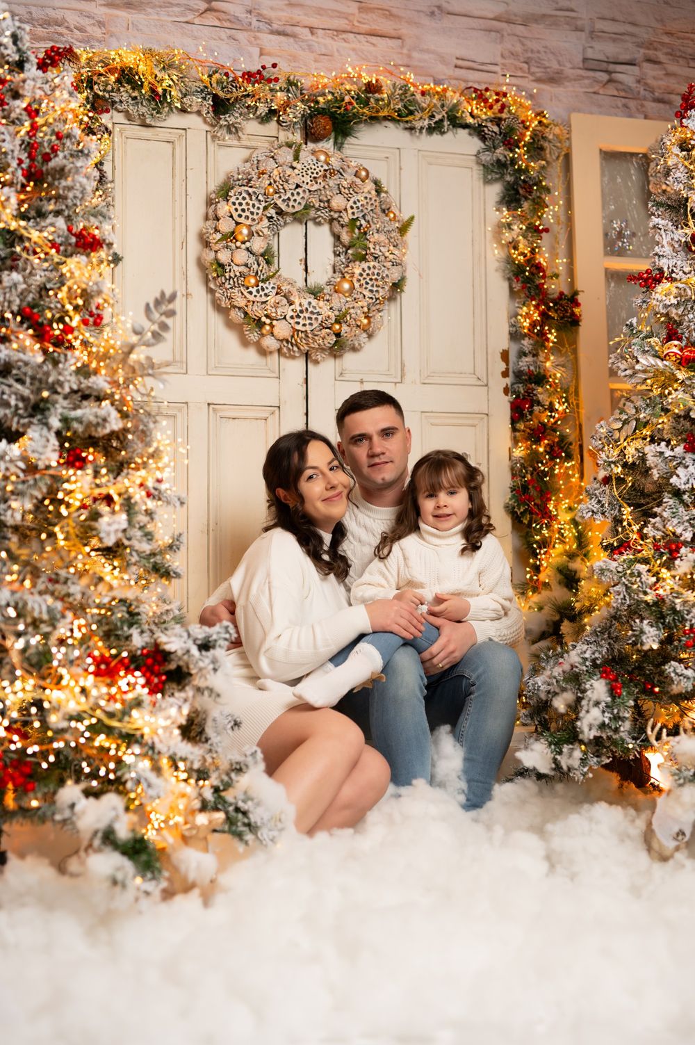 Festive Christmas photo set with a decorated white door, wreath, garlands, and artificial snow creating a cozy holiday scene.