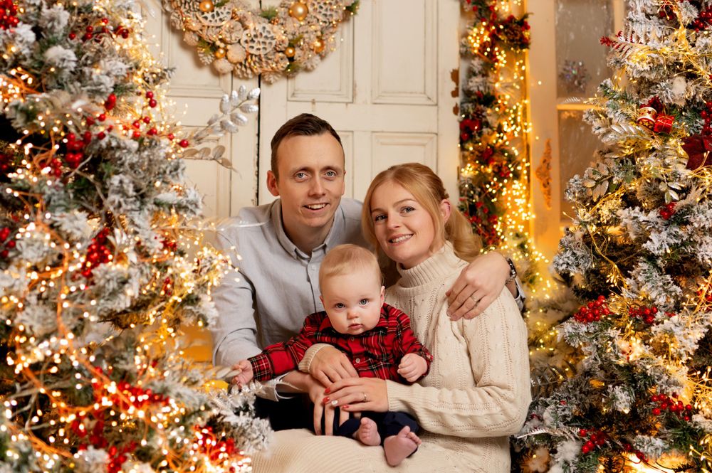 Warm holiday family portrait surrounded by Christmas decorations and twinkling lights.