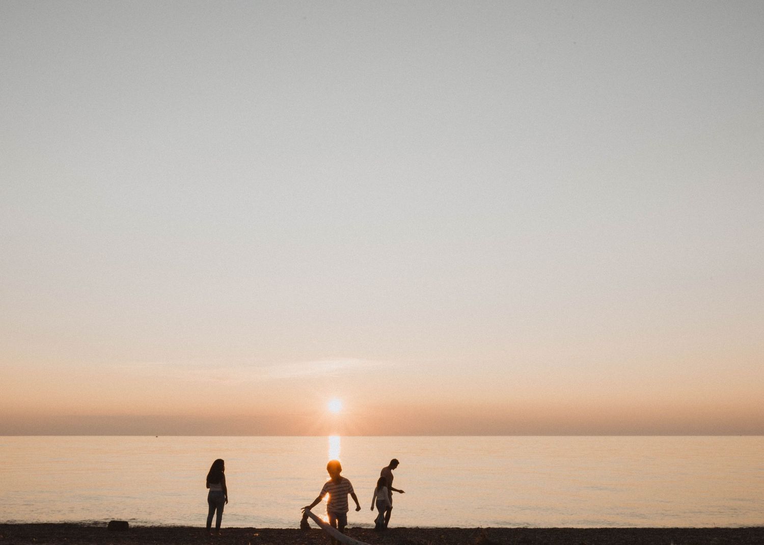 Family silhouettes playing together on beach during golden sunset over water.