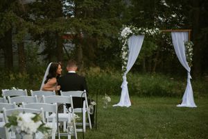Wedding ceremony setup with white chairs and decorative arches on a lush green lawn during an outdoor summer event.