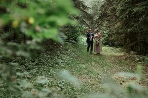 A couple stands together on a dreamy forest path surrounded by lush greenery and evergreen trees.