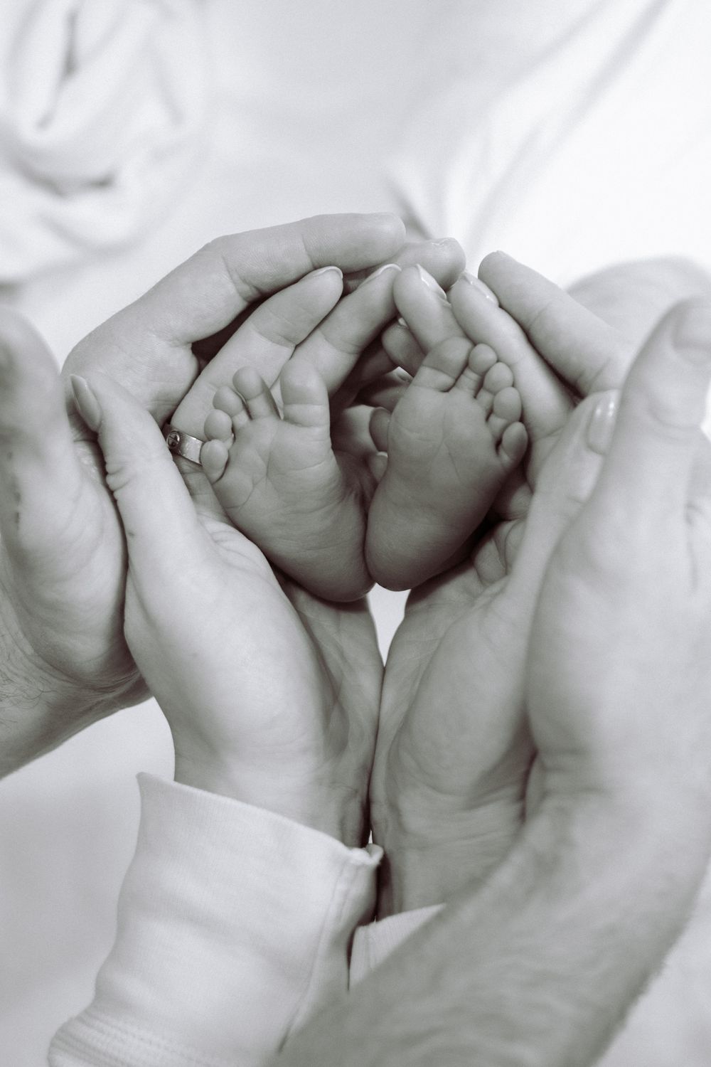 A tender black and white photograph showing tiny baby feet cradled gently in adult hands.